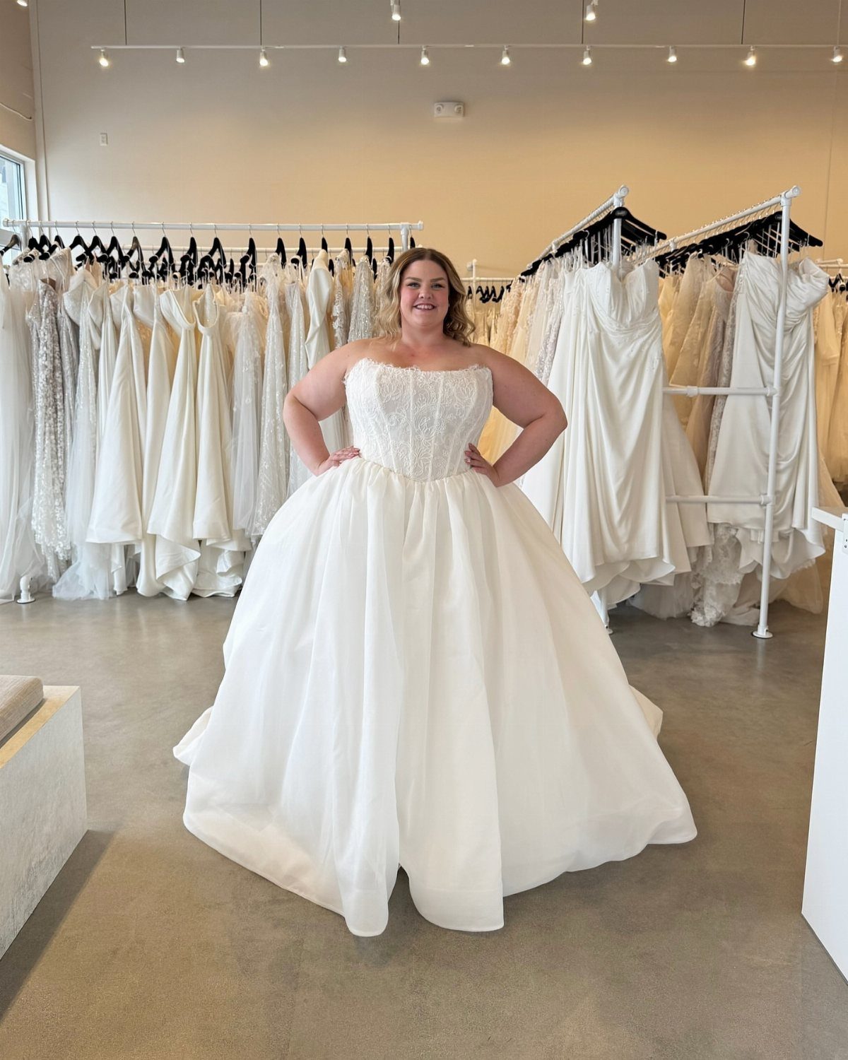 A woman wearing a white strapless ball gown wedding dress in a bridal shop.