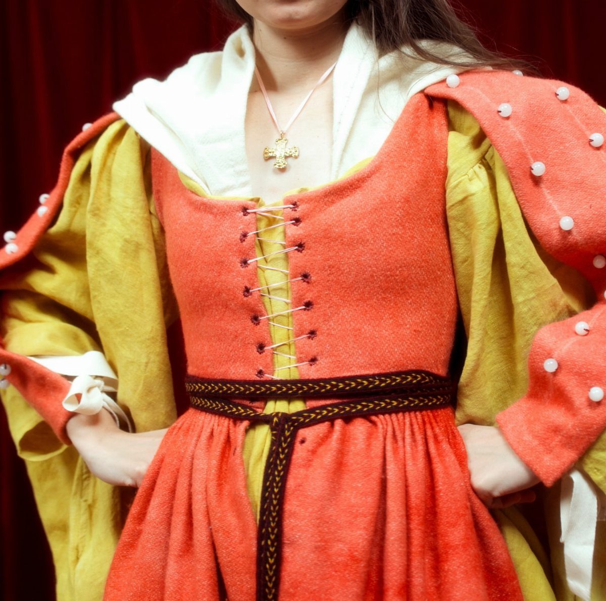 A person wearing a medieval orange and yellow gown with a dark braided belt.