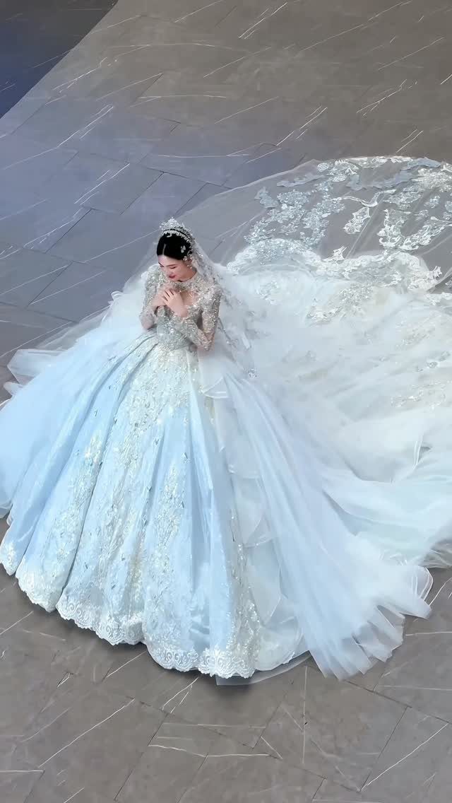 A woman in a voluminous light blue lace wedding dress with a long tulle train.