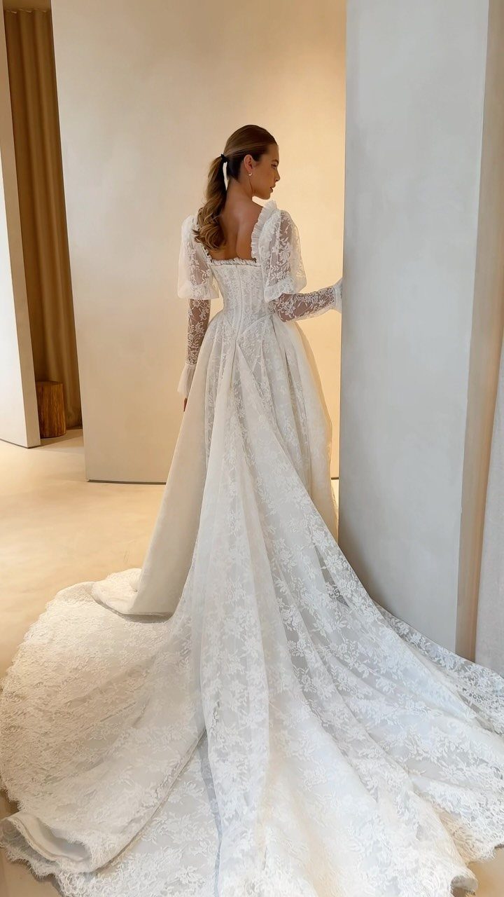Woman in a white lace wedding dress with long sleeves and a long train.