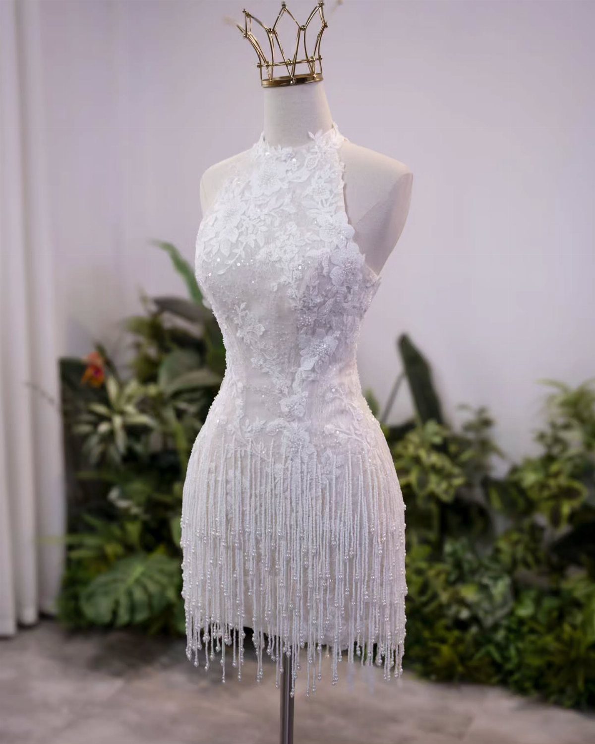 White lace halter dress with beaded fringe displayed on a mannequin wearing a gold crown.