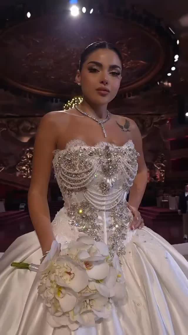 Woman in a heavily rhinestone-embellished white wedding gown holding white orchids.