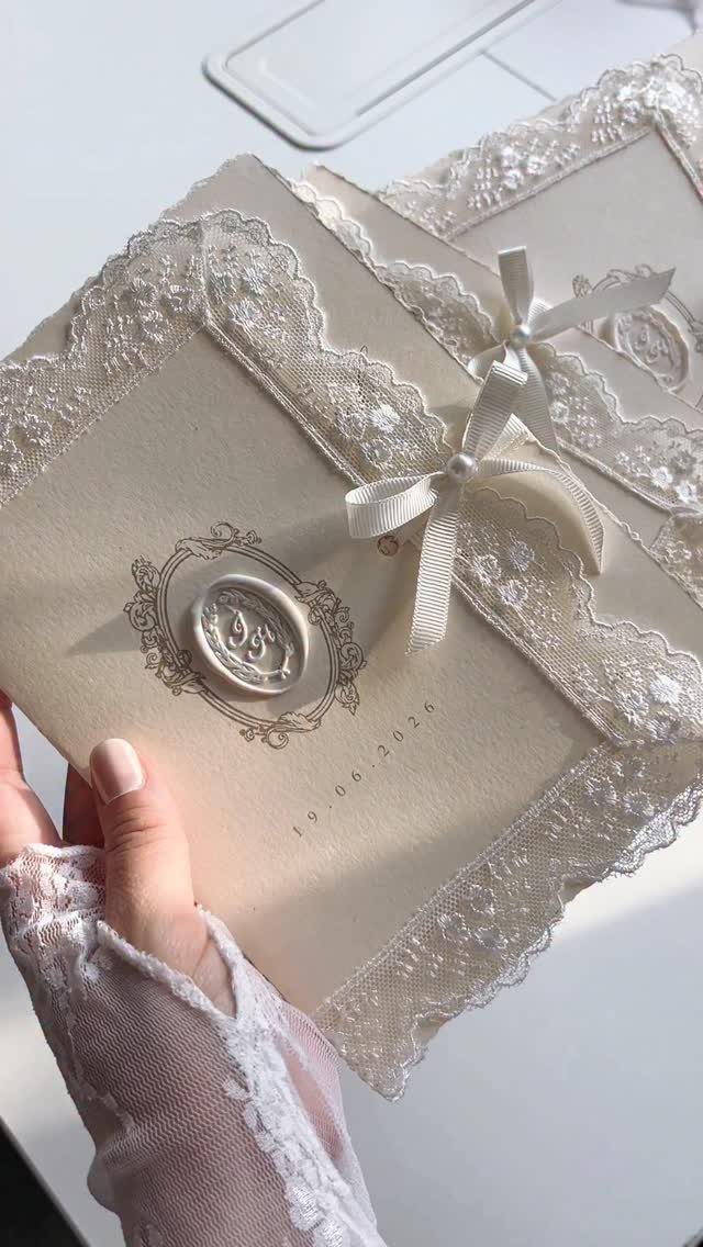 Shabby Chic Wedding: 10 Ideas for Timeworn Charm 4 A hand holding cream wedding invitations decorated with white lace, a satin bow, and a wax seal.