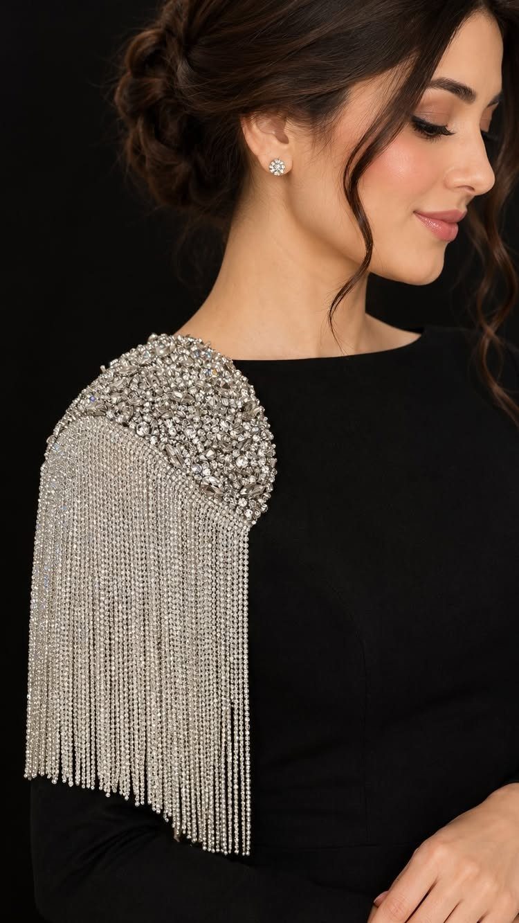 Woman wearing a silver crystal shoulder piece with long metallic fringe on a black garment.