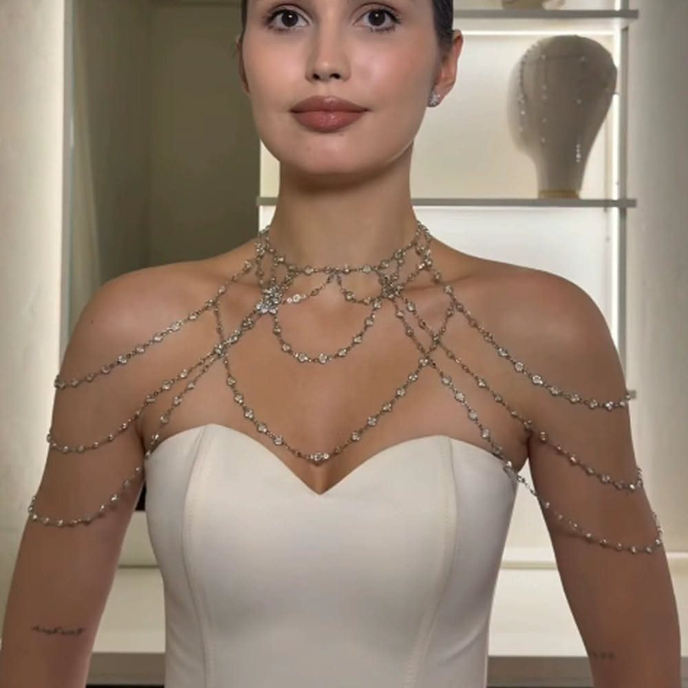 A woman wearing a sparkling crystal shoulder chain necklace over a white dress.