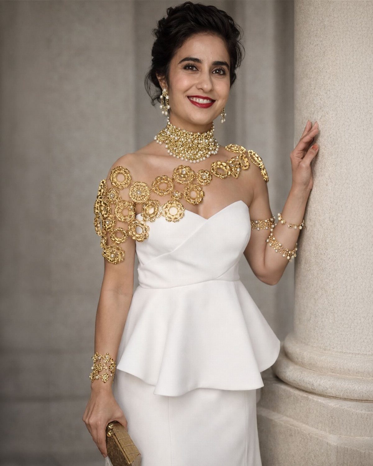 A woman wearing a white dress and ornate gold shoulder and neck jewelry.