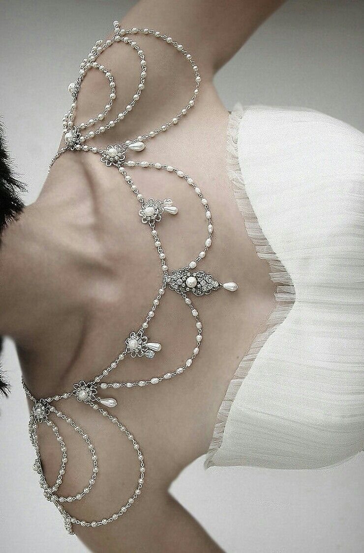 A vintage-style silver and pearl shoulder necklace draped over a person's collarbone and shoulders.
