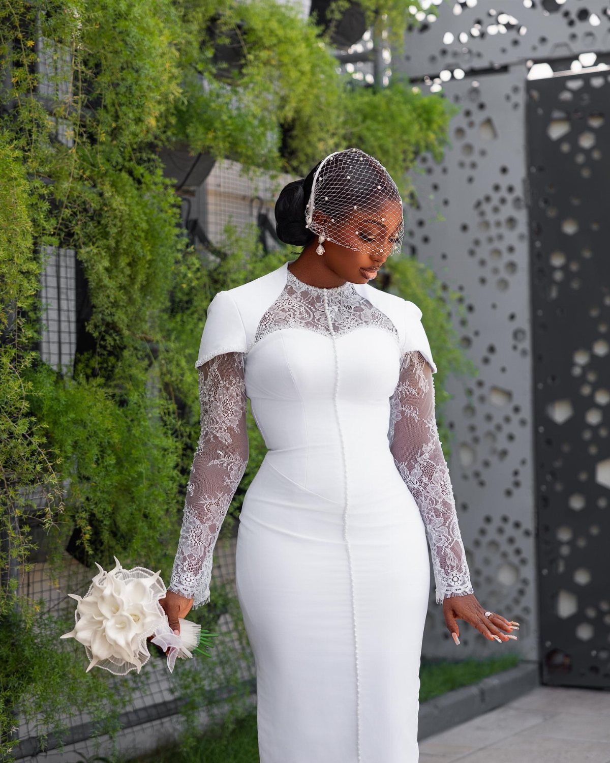 A woman wearing a white structured wedding dress with lace sleeves holding a bouquet.