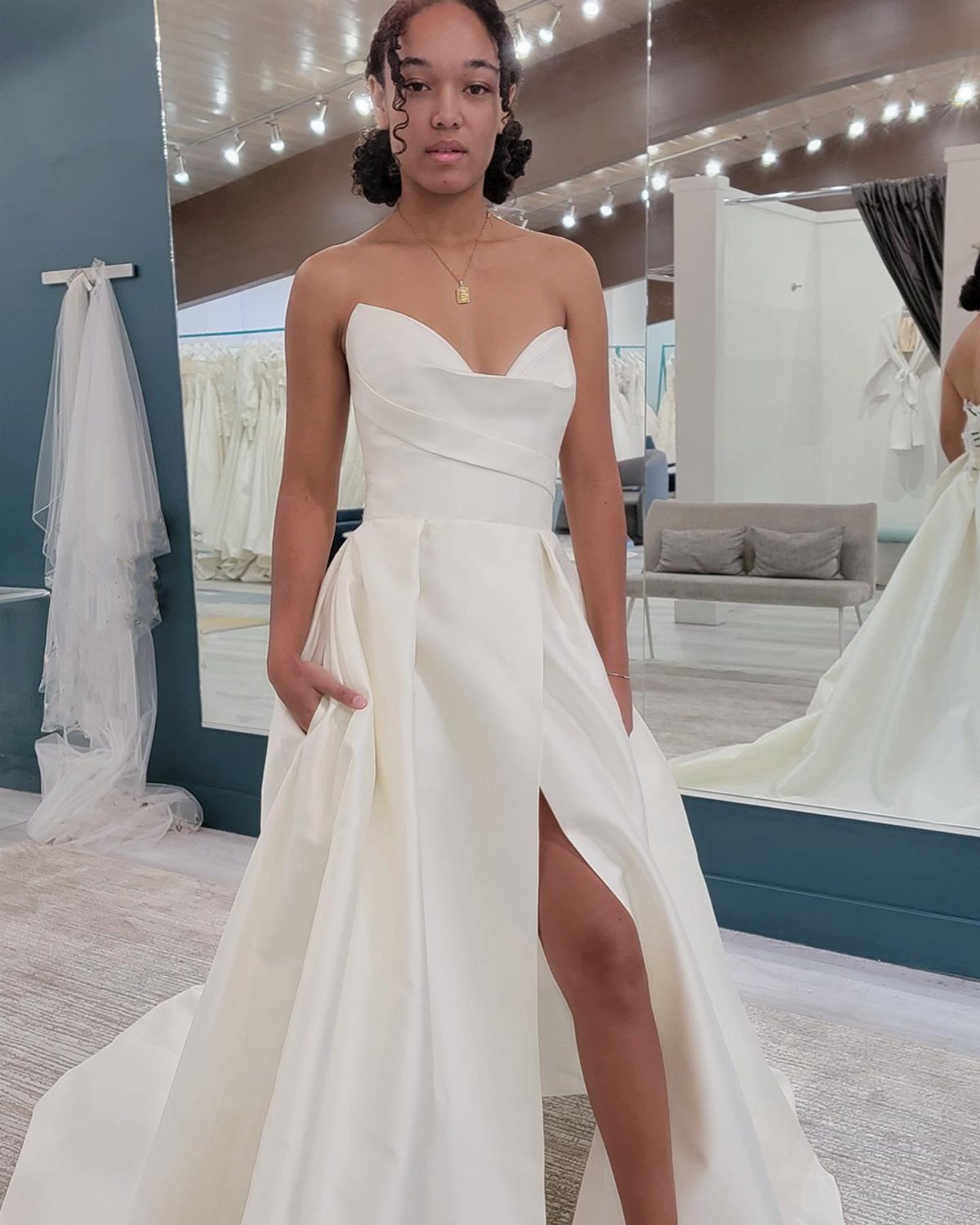 A woman wearing a structured white satin wedding dress with a sweetheart neckline and high slit.