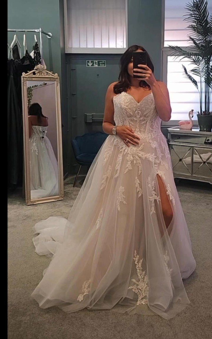 A woman in a white lace sweetheart wedding dress posing for a mirror selfie.