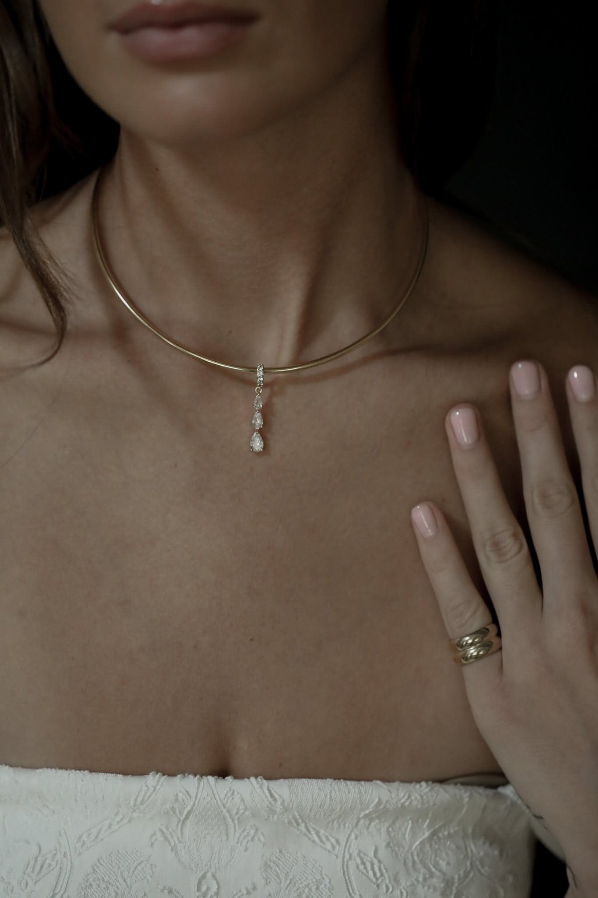 Gold collar necklace with a drop pendant worn with a white lace dress.