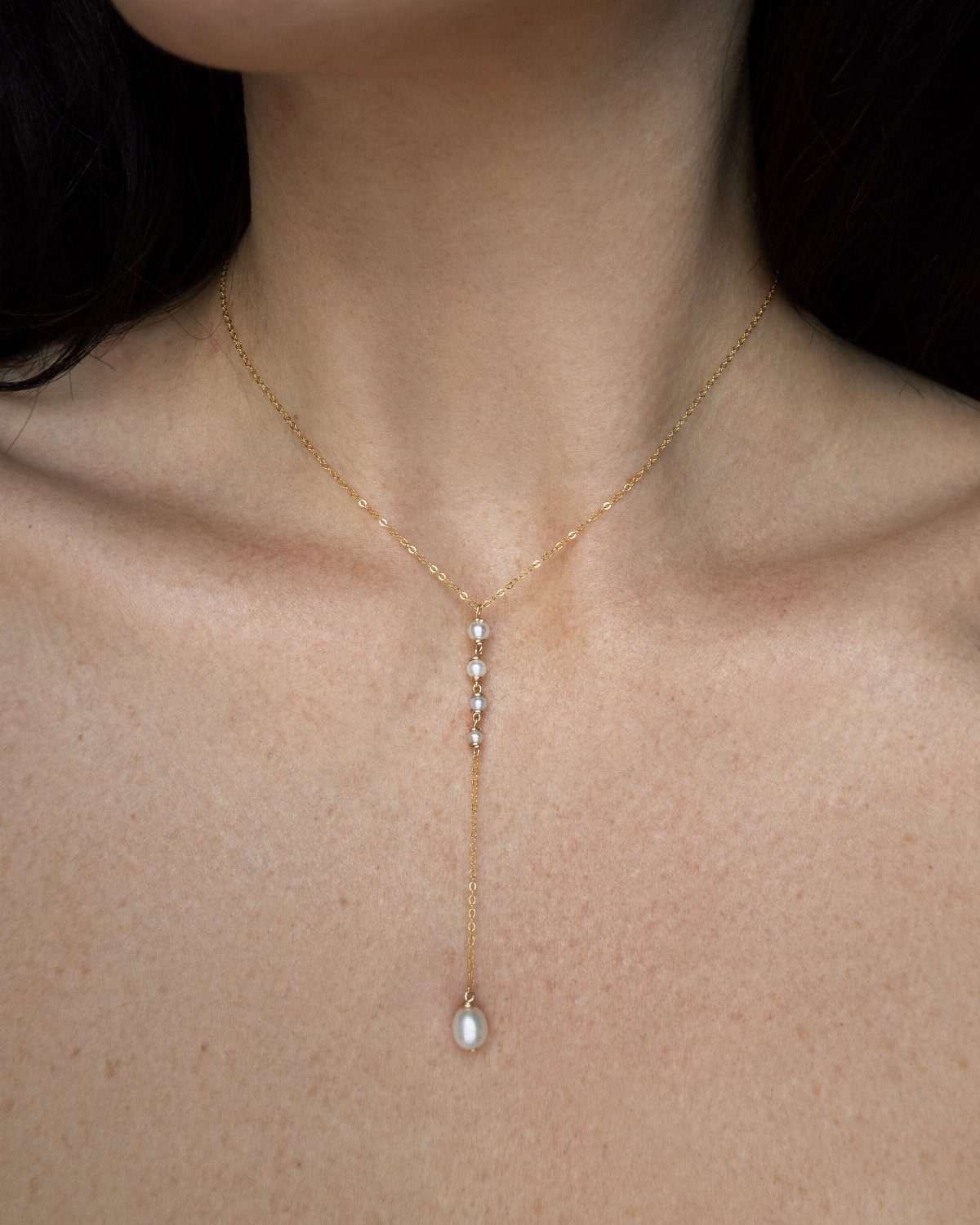 Thin gold chain necklace with pearl drop pendant on a person's neckline.