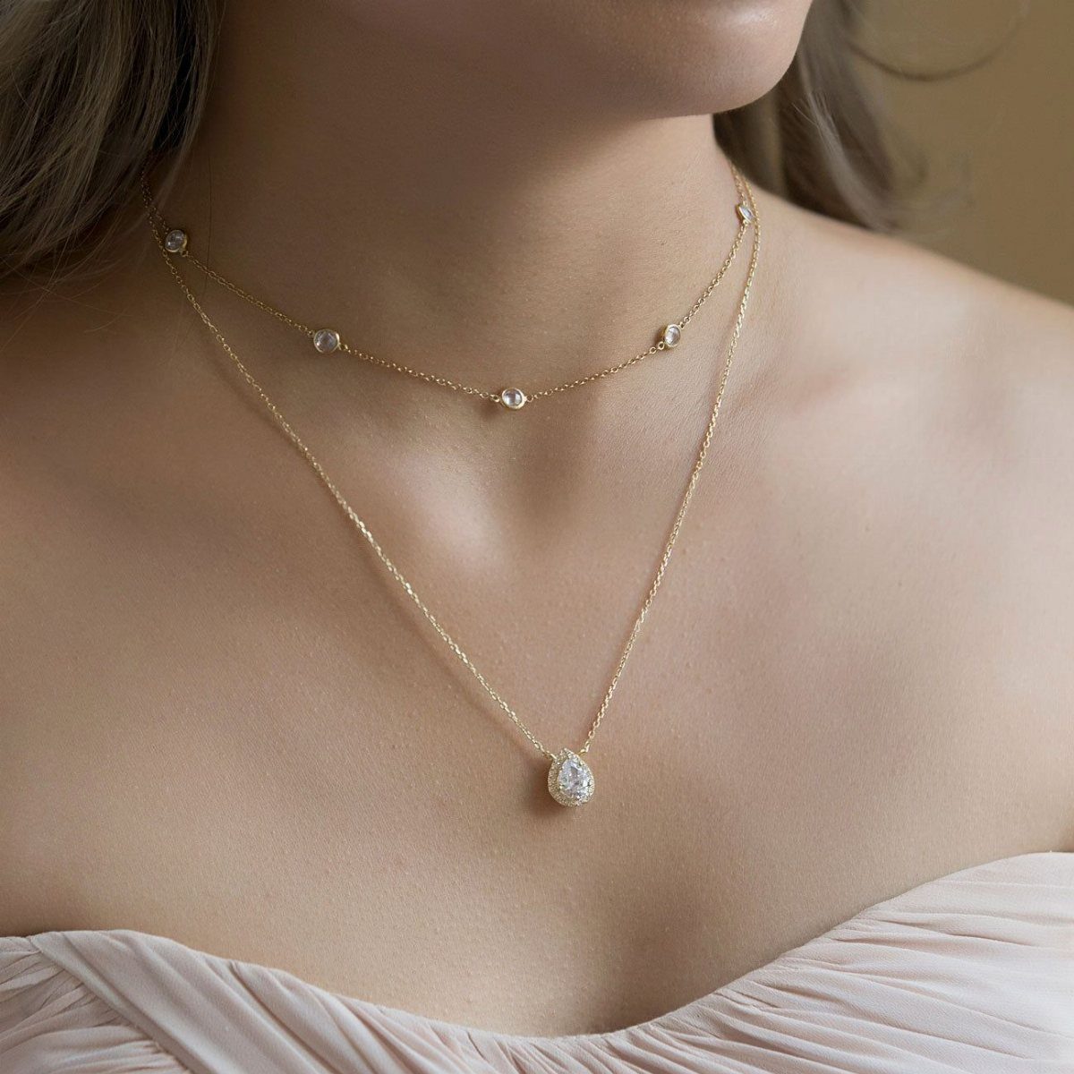 Gold layered necklaces with diamond accents on a person wearing a pink dress.