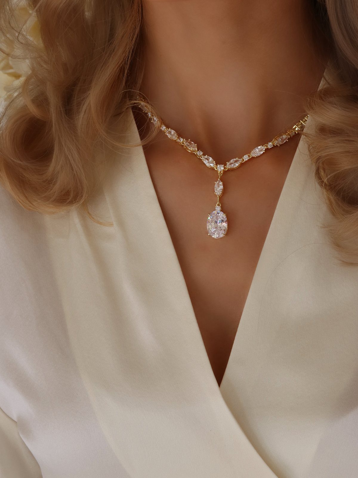 Gold necklace with an oval clear gemstone pendant worn with a white top.