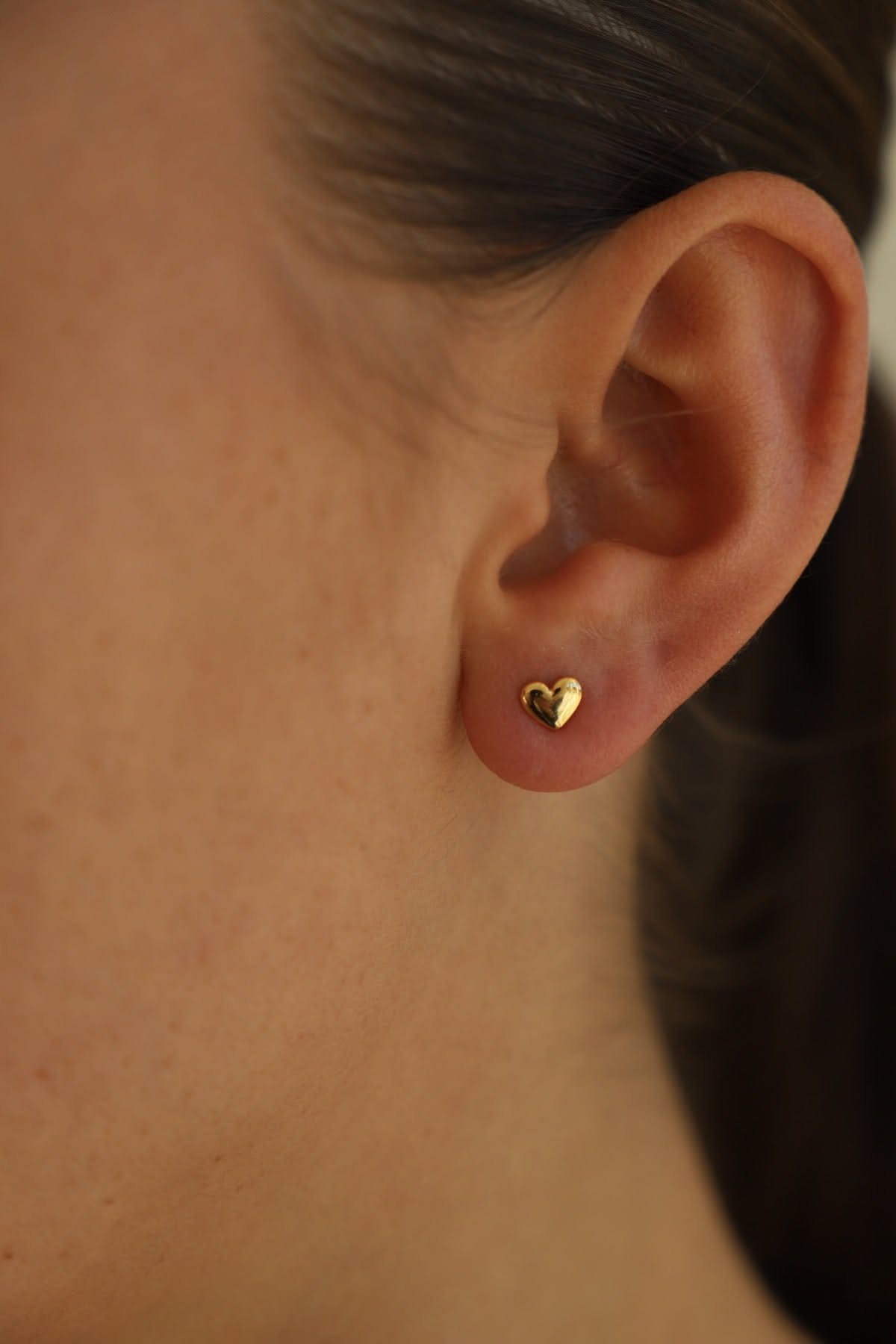 Small gold heart-shaped stud earring worn on a person's earlobe.