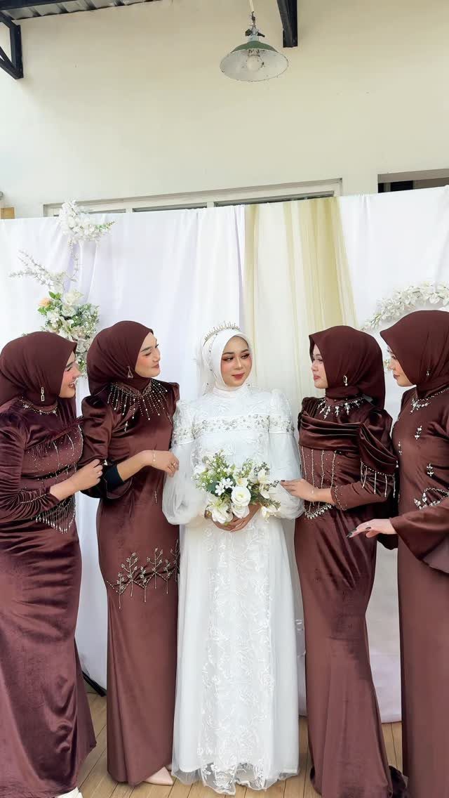 Women in brown velvet dresses and hijabs standing with a bride in white lace.