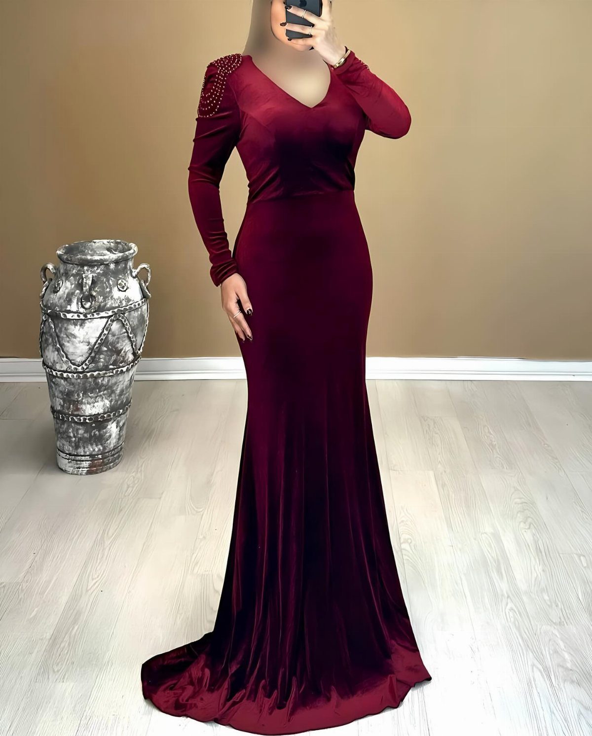 Person wearing a long-sleeved burgundy velvet V-neck maxi dress standing near a decorative urn.