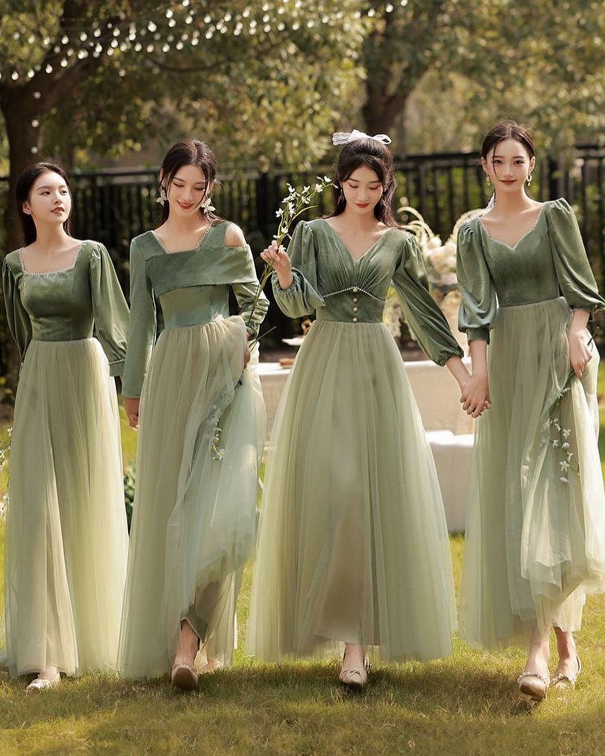 Four women wearing sage green velvet and tulle bridesmaid dresses standing in a garden.