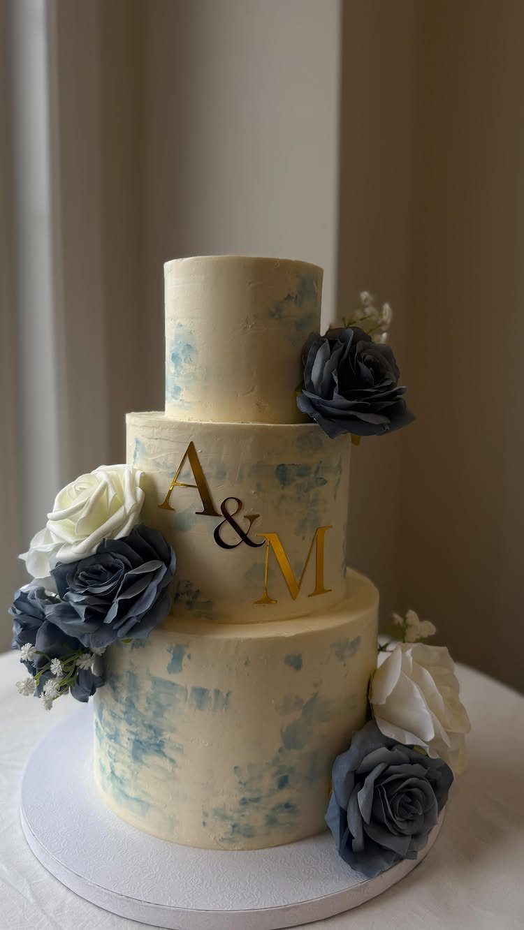 Wedding Cakes for 100 Guests: 6 Designs That Actually Work 1 A three-tier wedding cake decorated with blue watercolor accents and white and blue roses.