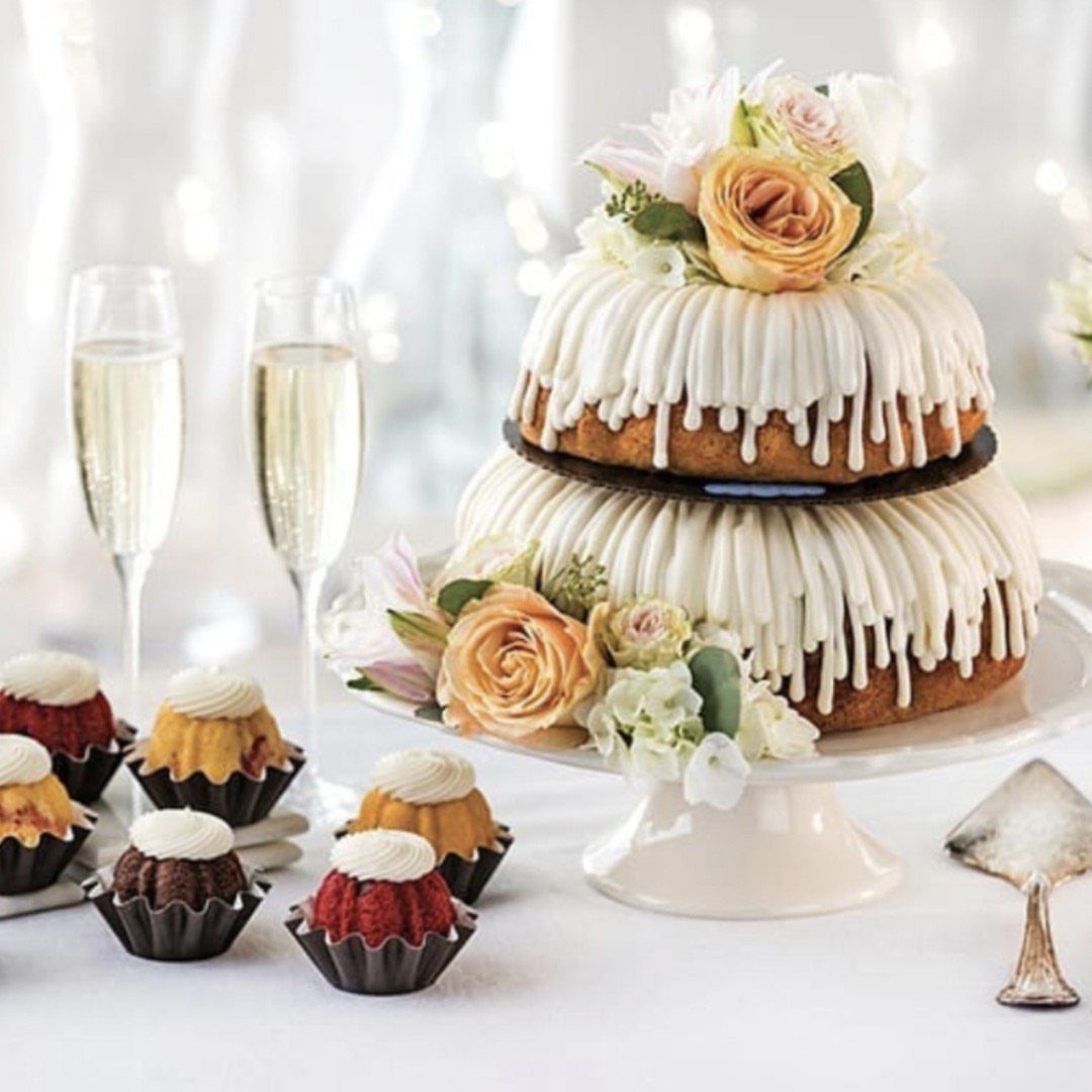 Wedding Cakes for 100 Guests: 6 Designs That Actually Work 3 Two-tiered bundt cake with white icing and peach roses on a white cake stand.