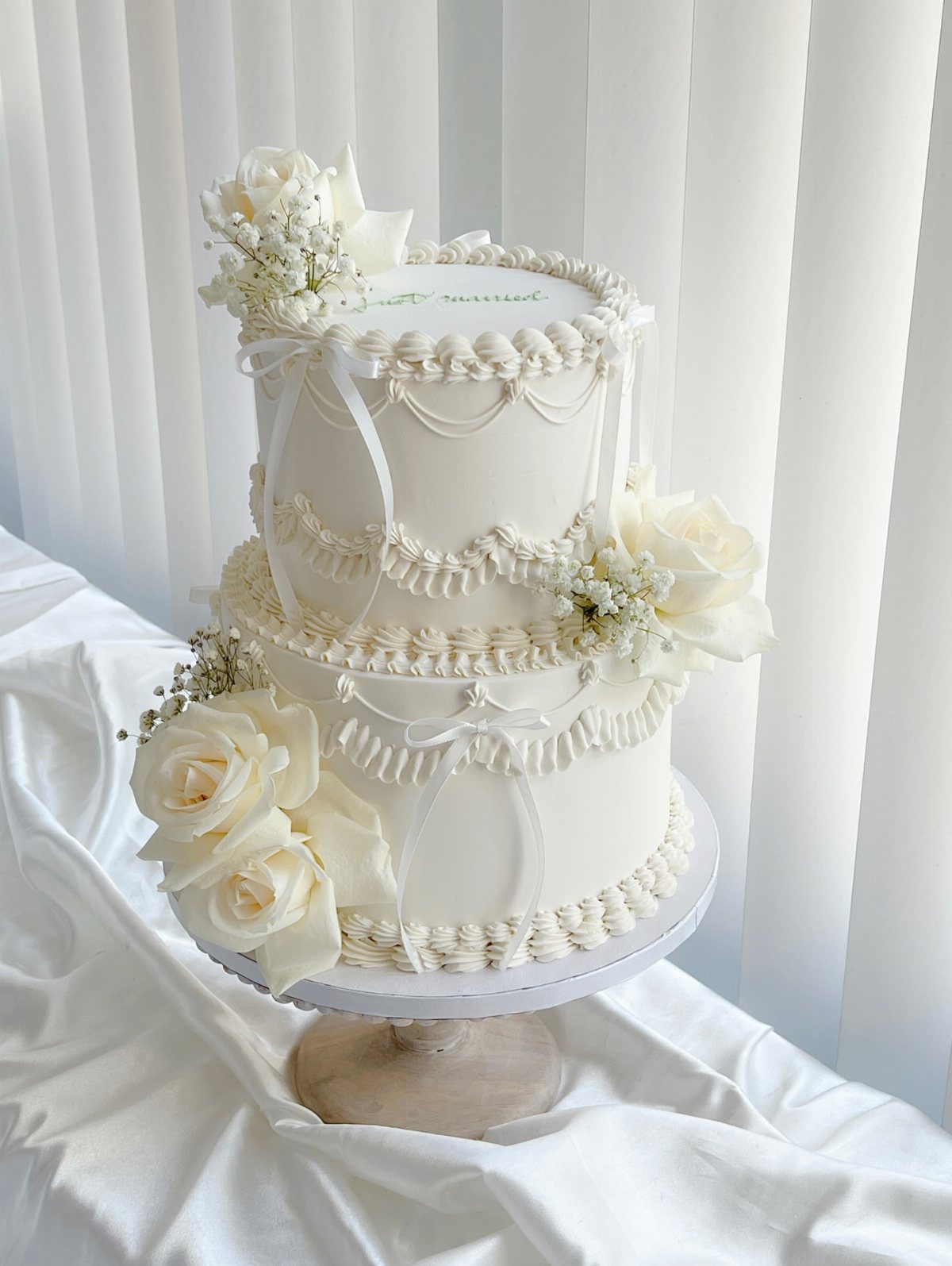 Wedding Cakes for 100 Guests: 6 Designs That Actually Work 6 A two-tier white wedding cake decorated with elegant frosting patterns and large white roses.