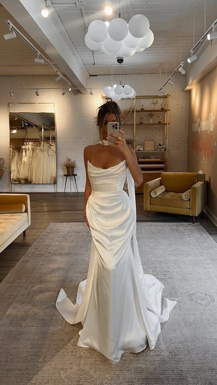 Woman in a white satin wedding dress with a draped neckline posing in a bridal boutique.