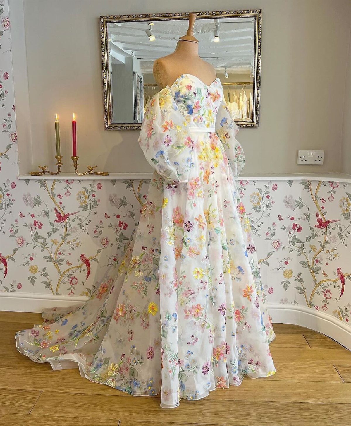Floral print wedding dress with large puff sleeves displayed on a mannequin against floral wallpaper.