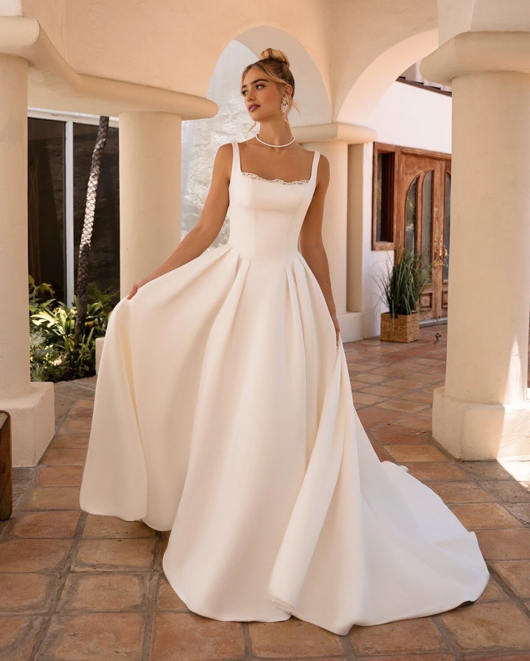 A woman wearing a white satin wedding dress with thick straps and a full skirt.