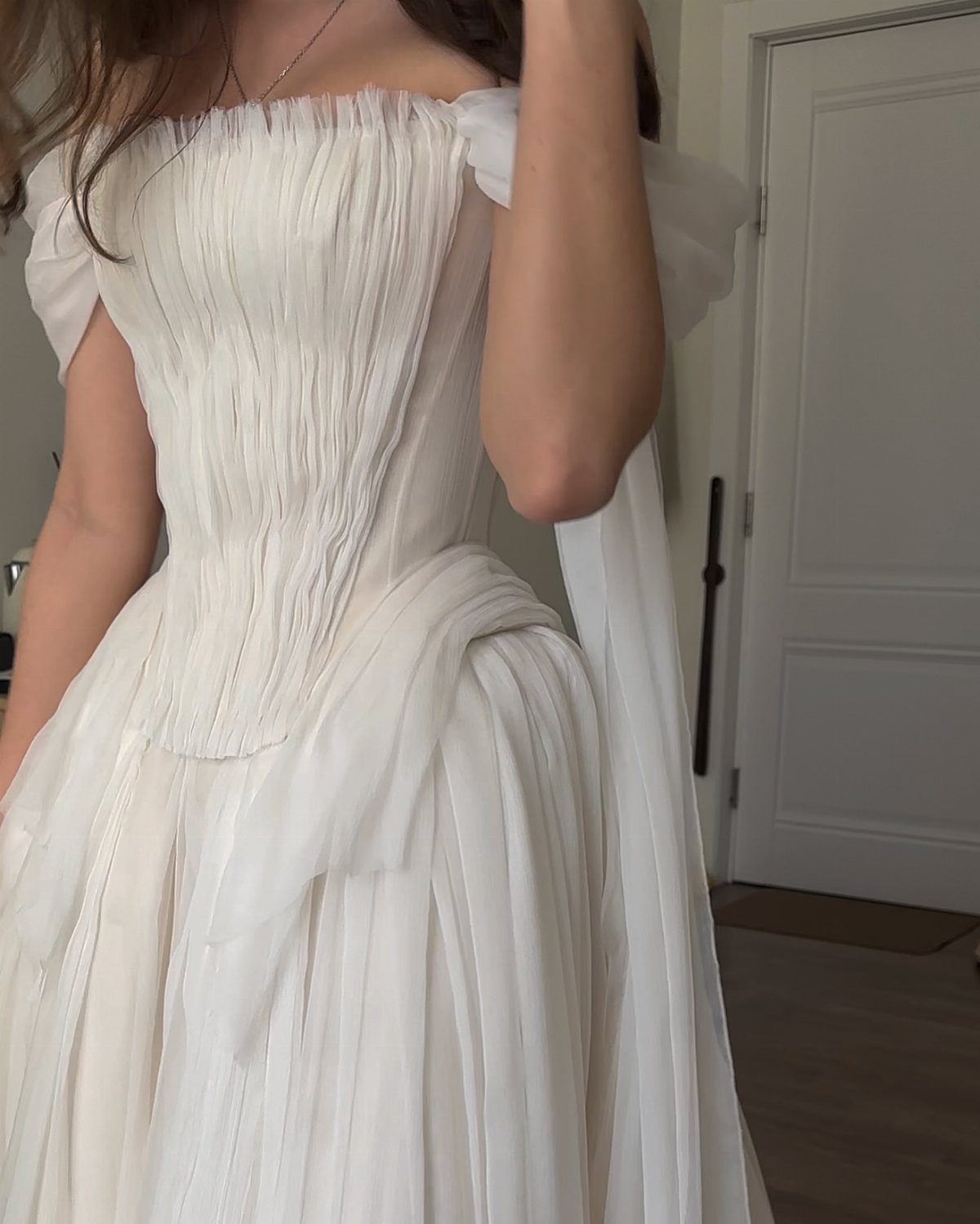 A woman wearing a white pleated off-the-shoulder wedding dress with a flowing skirt.