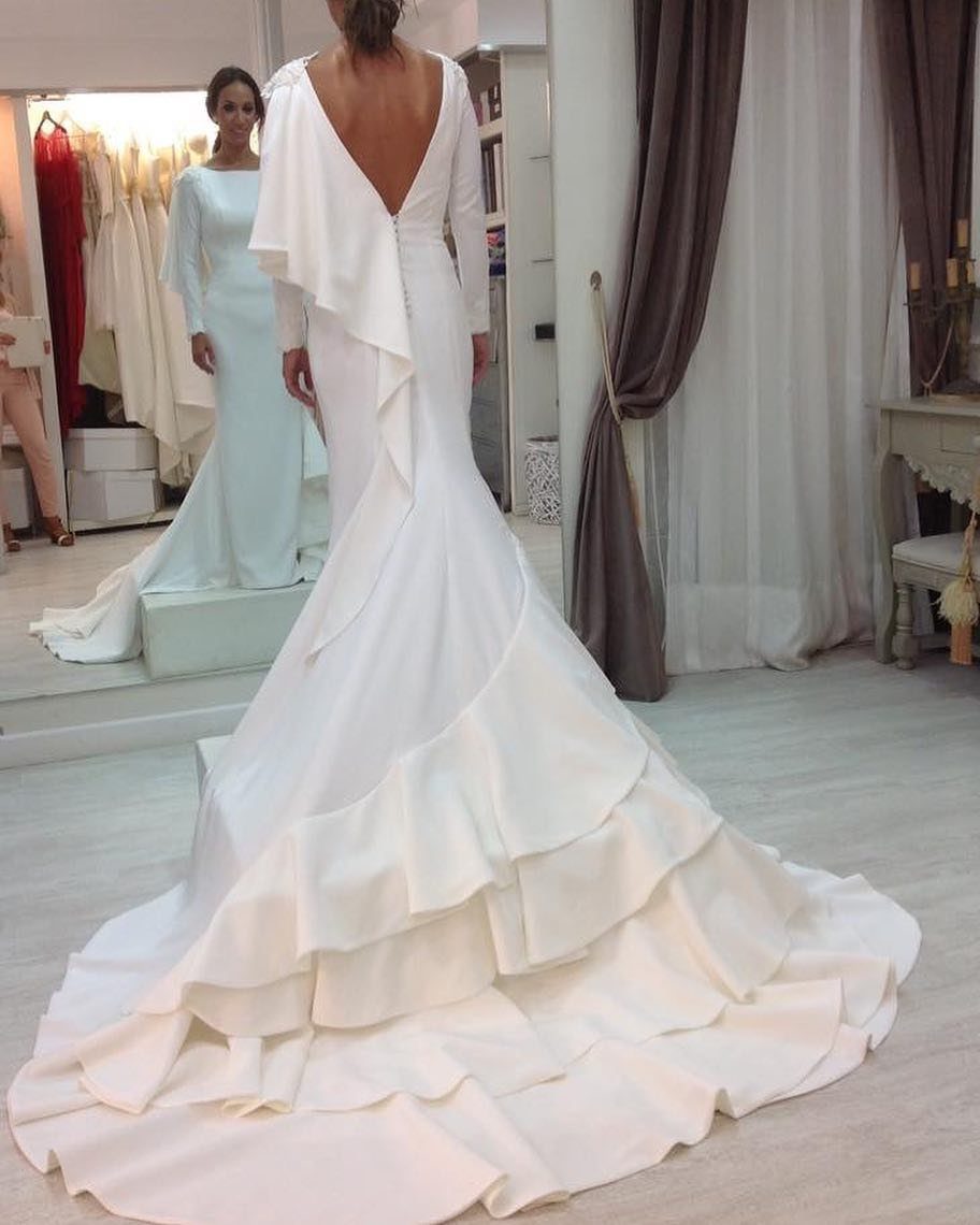 Woman in a white mermaid wedding dress with tiered ruffles and a deep V-back.