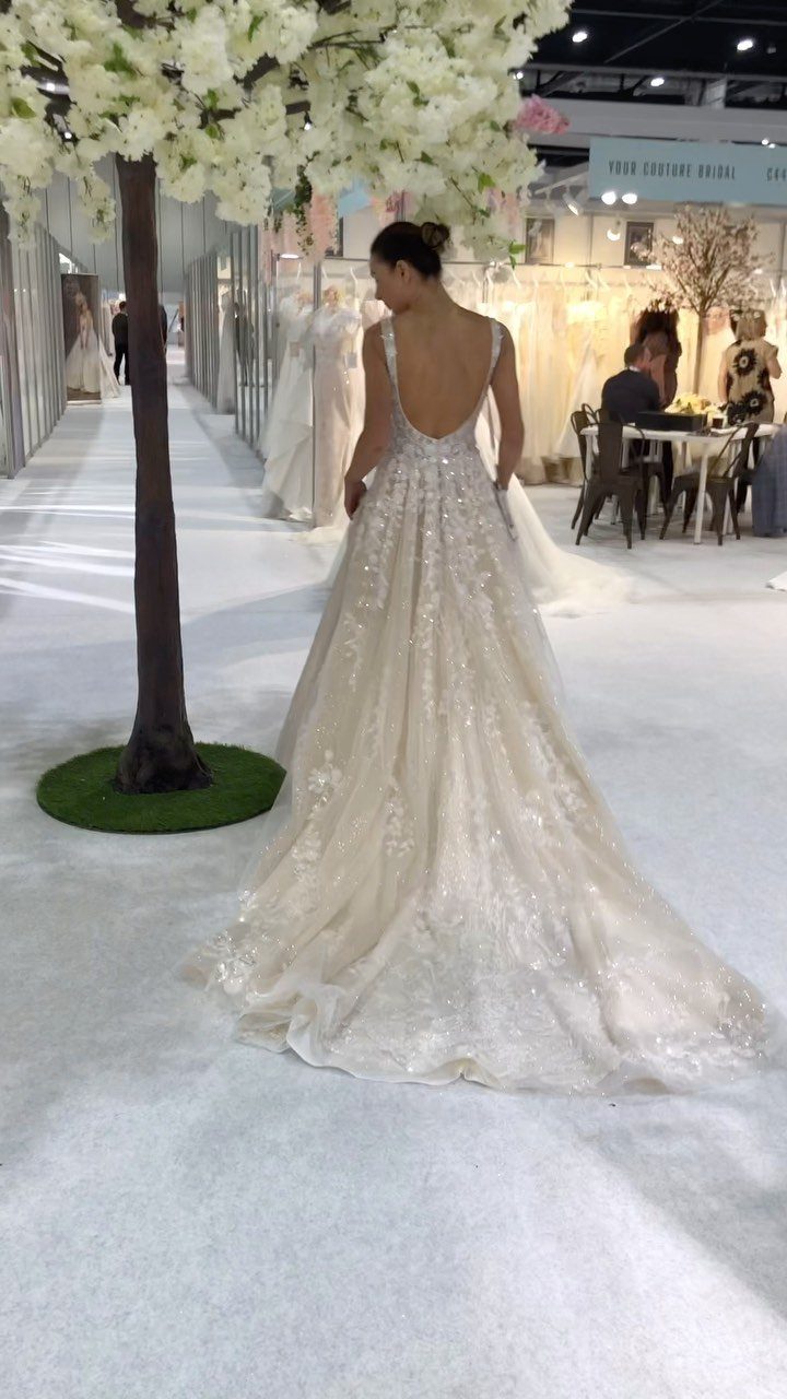 A woman wearing a sparkling white A-line wedding dress with a low back in a showroom.