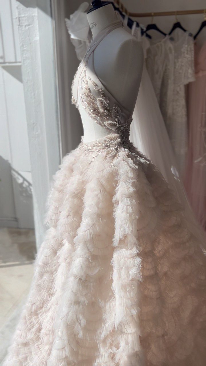 A cream wedding gown with a beaded bodice and voluminous ruffled skirt on a mannequin.