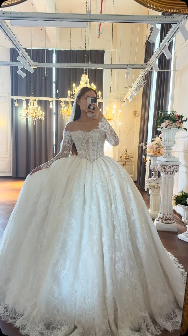 A woman in a voluminous white lace wedding gown posing for a mirror selfie.