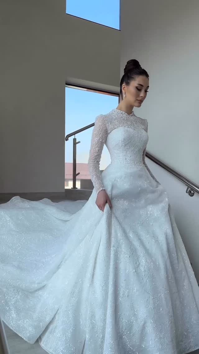 A woman wearing an elegant long-sleeved lace wedding gown standing on a staircase.