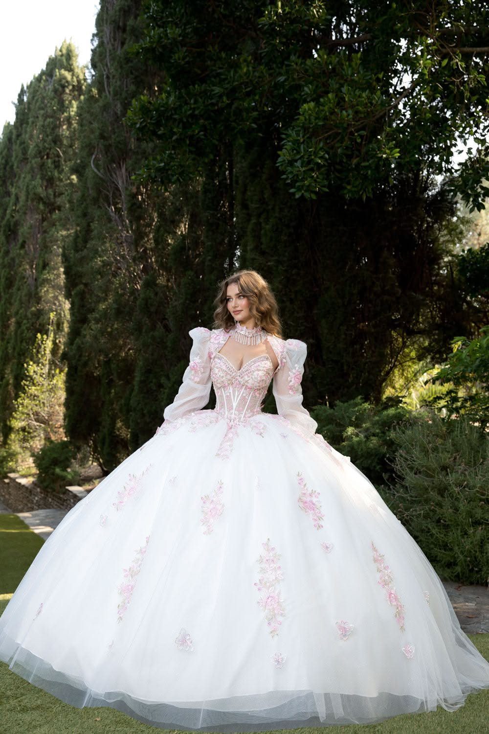 Wedding Dress White and Pink: 8 Gowns for a Colorful Ceremony 3 Woman in a white ballgown with pink floral appliqués standing in a lush green garden.