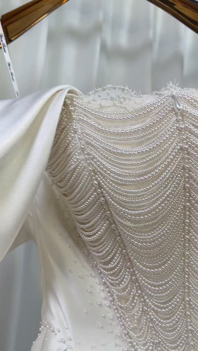 Close-up of a white wedding dress adorned with many draped strands of small pearls.