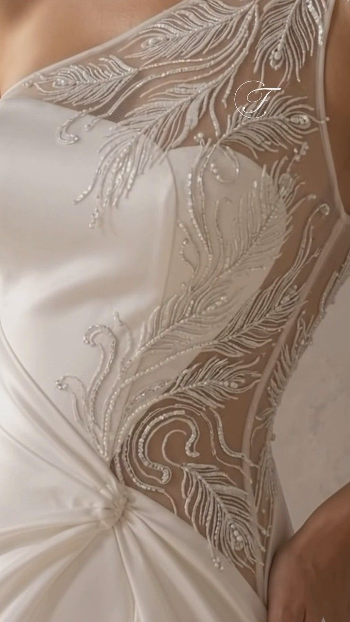 Close-up of a white wedding dress with feather-shaped pearl embroidery and draped satin fabric.