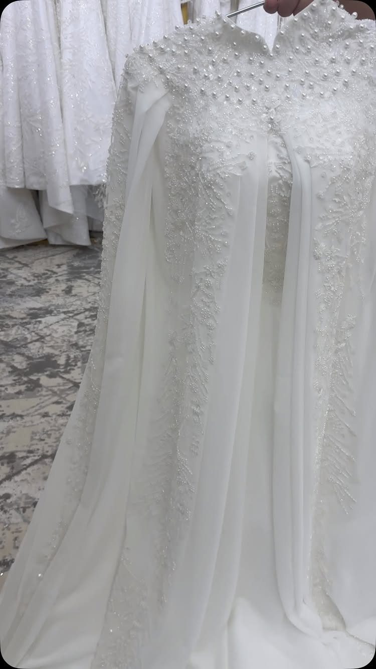 White wedding dress with intricate lace and pearl details on the bodice and neckline.