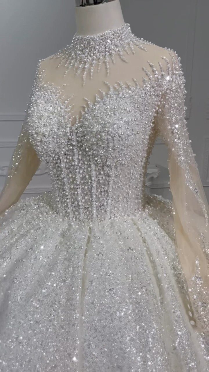 A white wedding dress heavily embellished with pearls and beads on a mannequin.