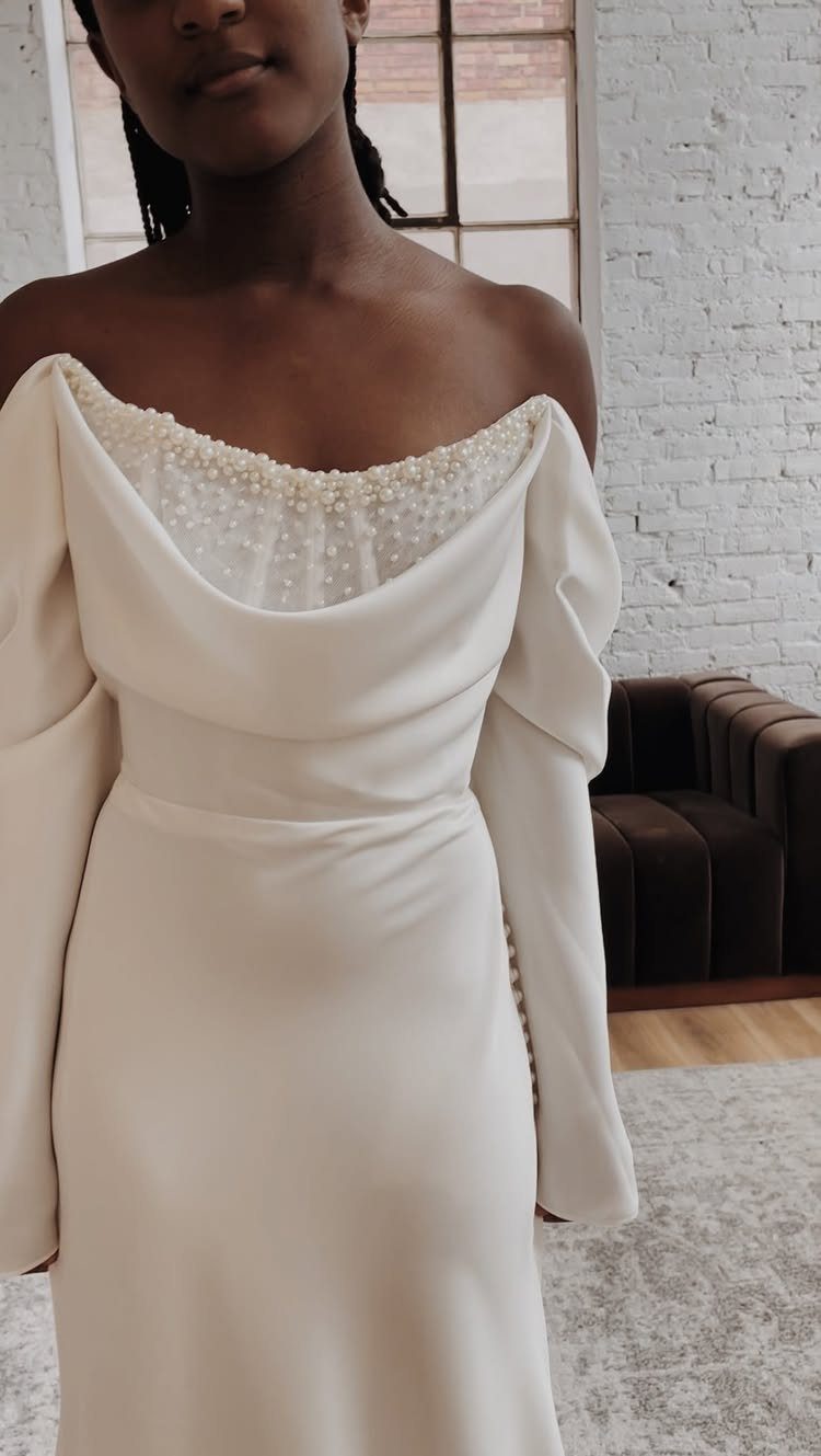 A woman wearing an off-the-shoulder cream wedding dress with pearl details on the neckline.
