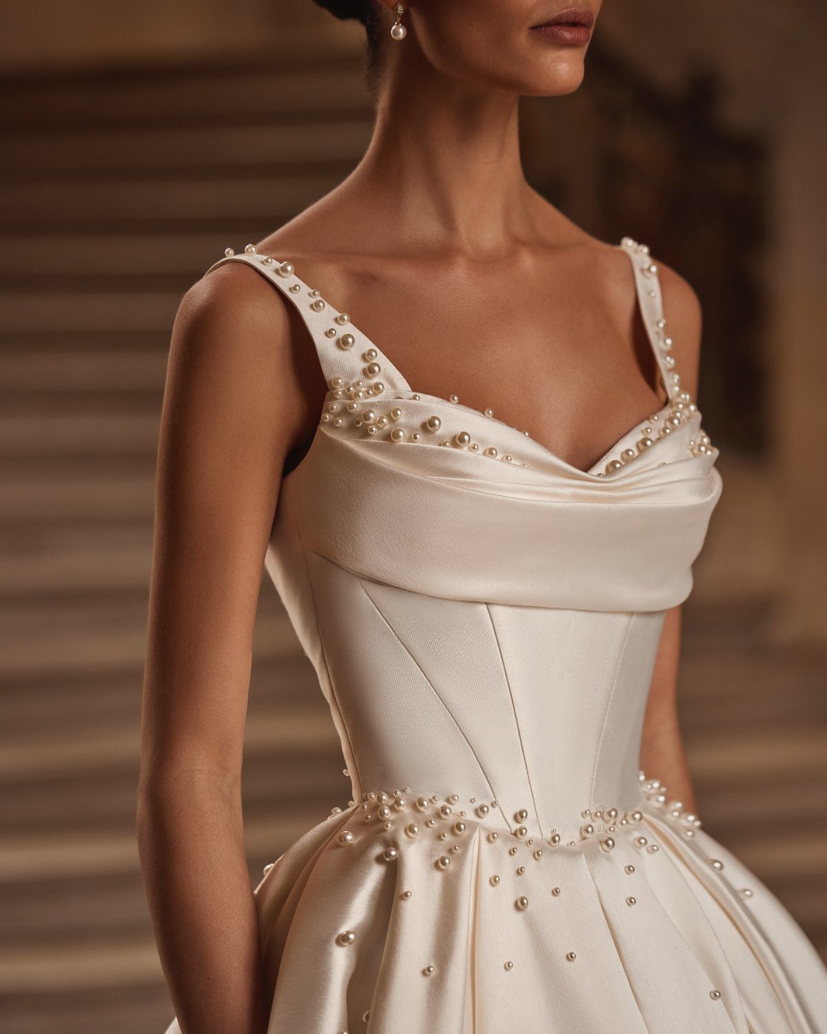 Woman wearing an ivory satin wedding dress with pearl details on the straps and bodice.