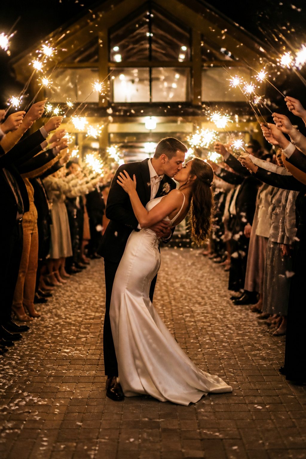 A couple exiting the venue through a tunnel of sparklers at night.