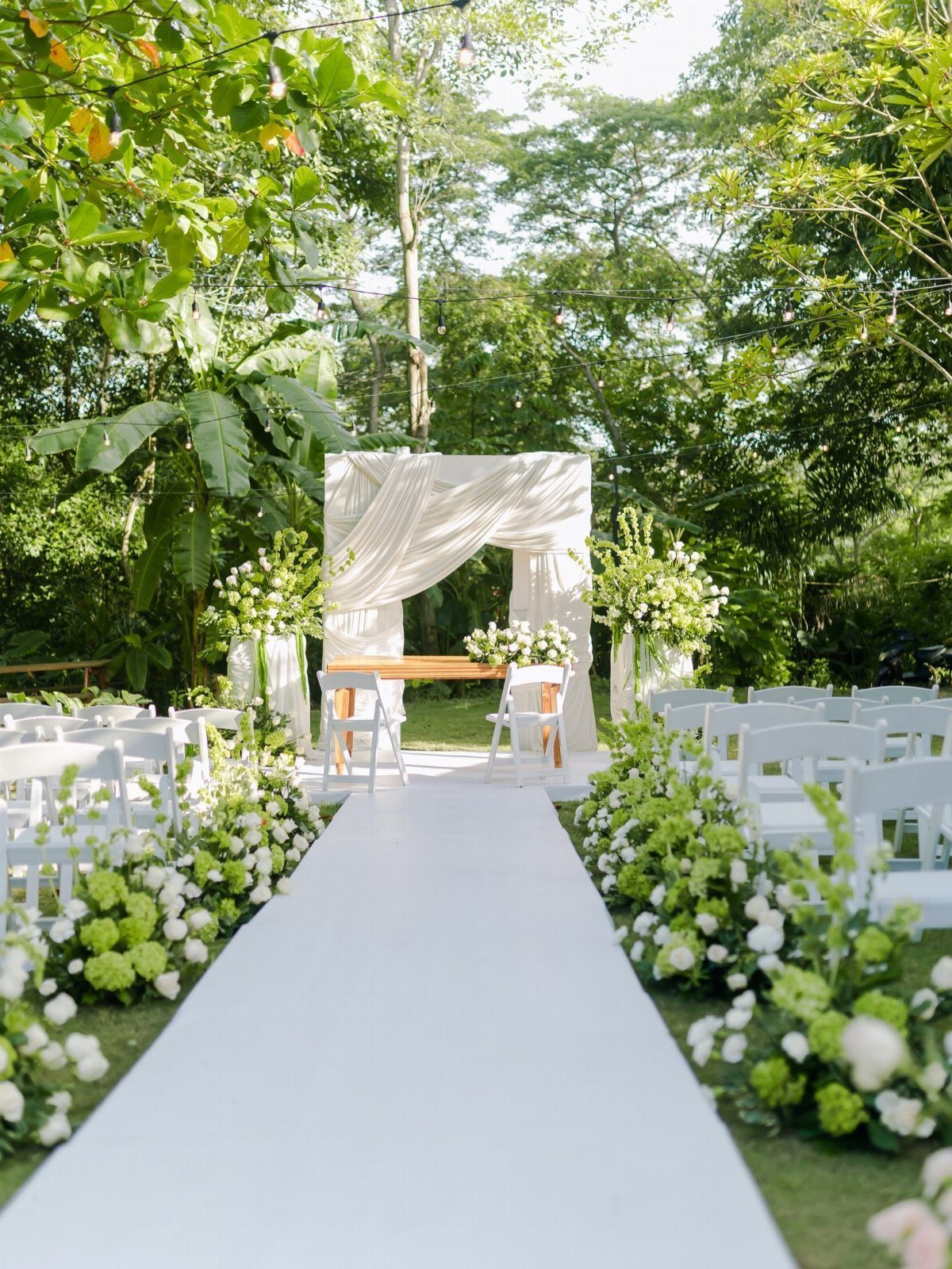 White wedding aisle with runner leading to a draped fabric altar in a garden.