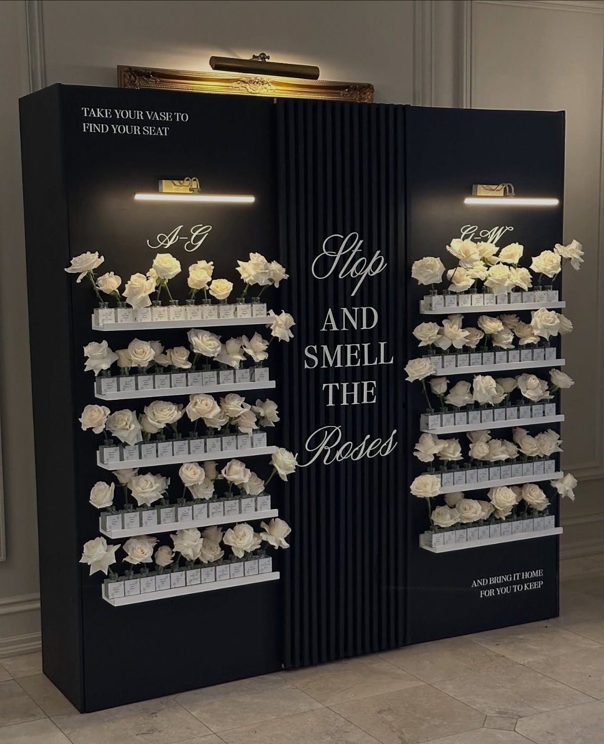 Black wall display with white roses in small vases and decorative white text.