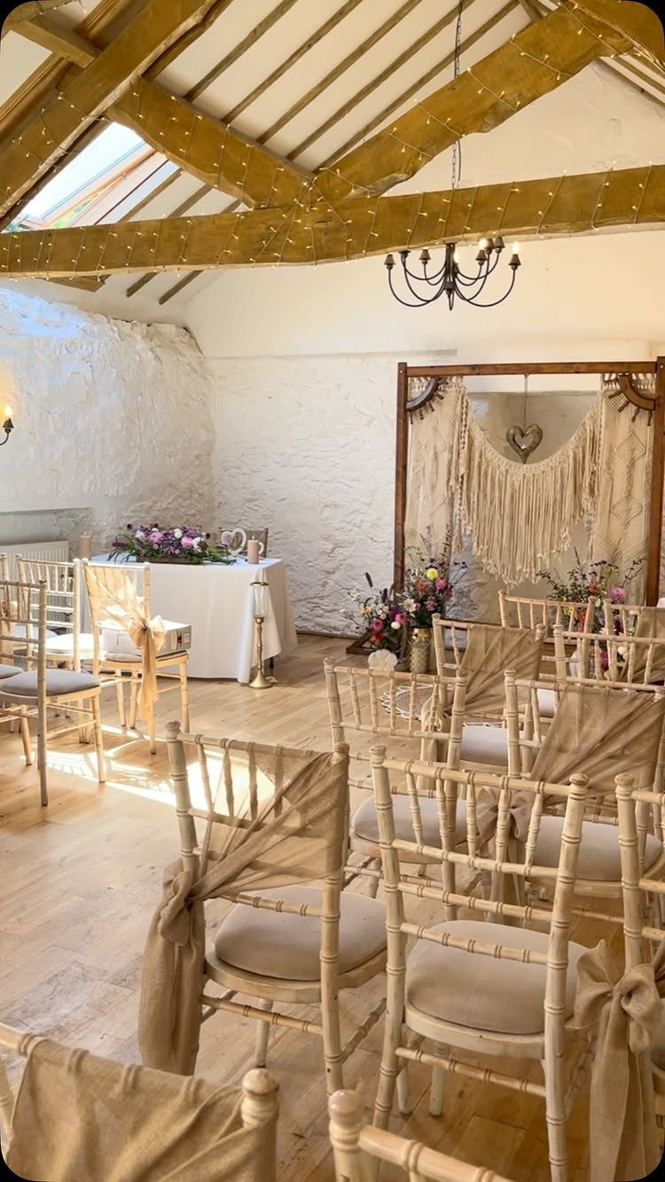 Wedding ceremony setup with wooden chairs and a large macramé backdrop in a rustic room.