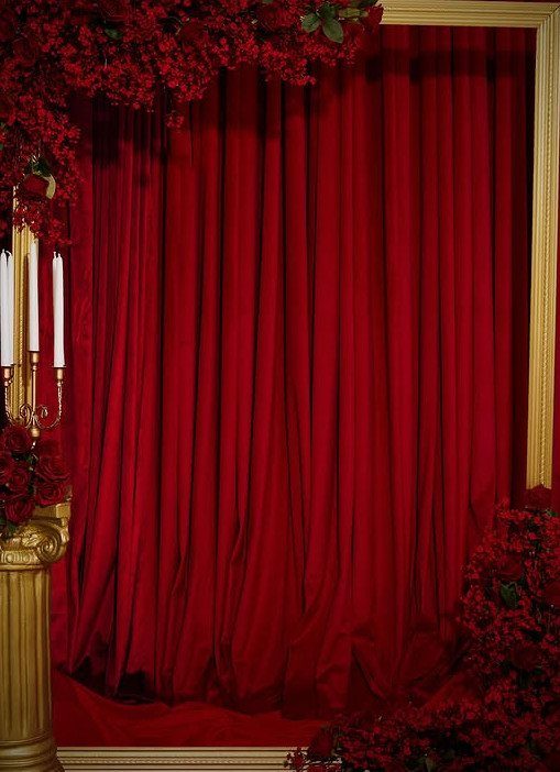 Red velvet curtains framed by gold borders and dark red floral arrangements.