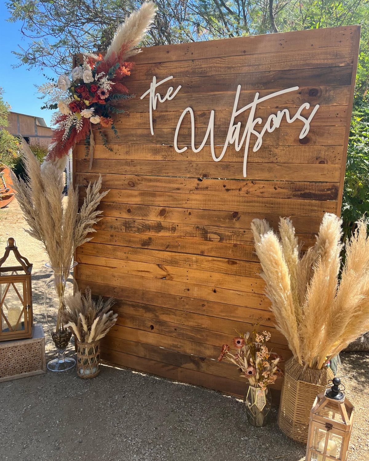 A rustic wooden plank backdrop decorated with pampas grass and floral arrangements for a wedding.