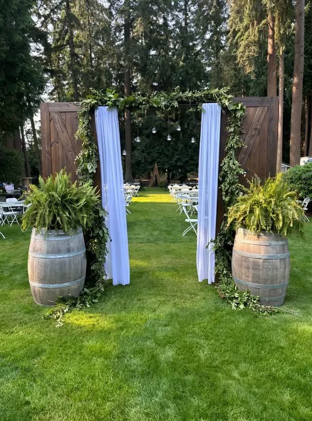 Large wooden doors decorated with greenery and white fabric serve as a wedding ceremony entrance.
